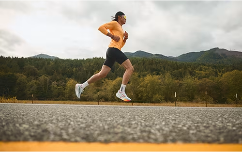 Pessoa correndo em uma estrada com montanhas e árvores ao fundo em um dia nublado